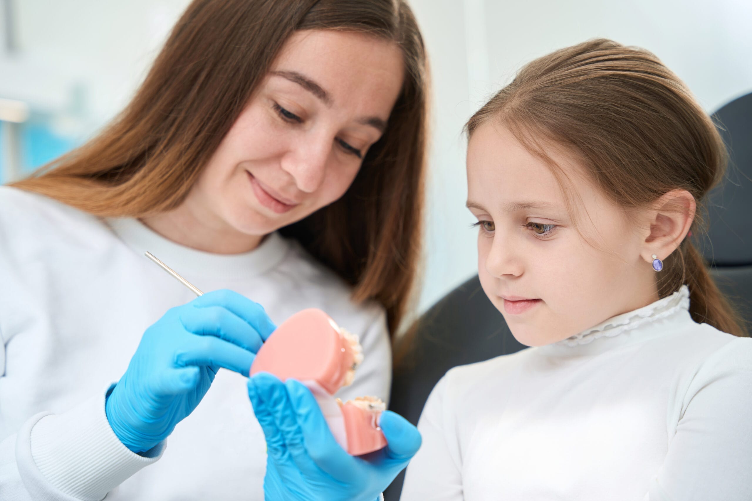 Smiling pedodontist showing structure of teeth on dental model to focused kid